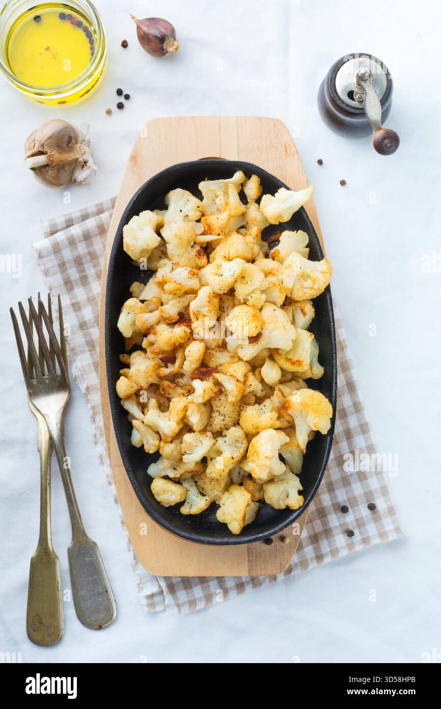 Cavolfiore al forno con spezie e aglio in una padella in ghisa su uno sfondo chiaro. Messa a fuoco selettiva.Vista superiore. Foto Stock