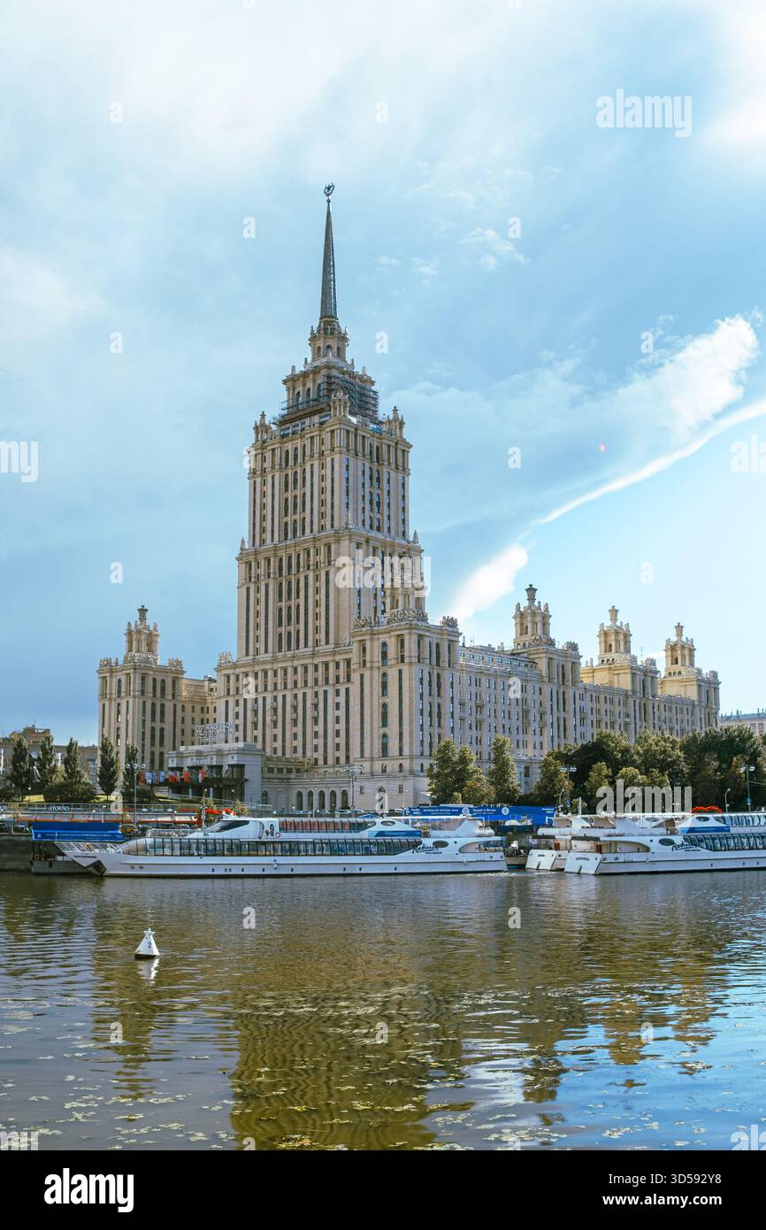 25 agosto 2025, Mosca, Russia. Uno splendido grattacielo si erge alto vicino al fiume, riflettendo la sua grandezza sull'acqua, mentre le barche scivolano pacificamente Foto Stock