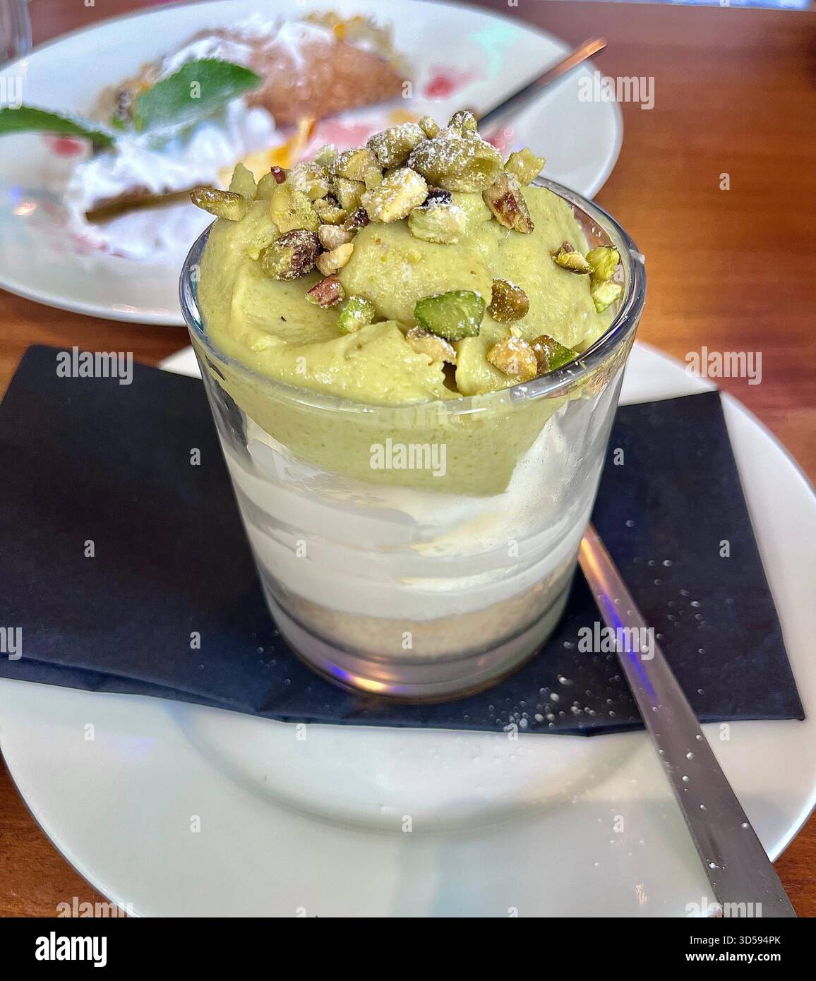 Primo piano di un dessert al pistacchio a strati servito in una tazza di bicchiere in una caffetteria di Hull, in Inghilterra. Il piatto presenta consistenze cremose con noci e presen Foto Stock