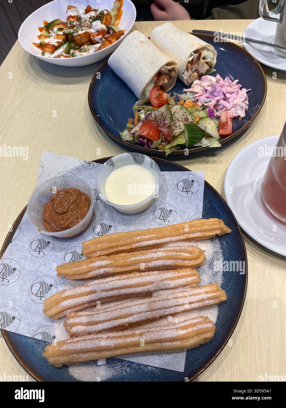 Tavolo del ristorante con churros dorati spolverati di zucchero servito con salsa di cioccolato, involtini mediterranei e insalata fresca su piatti di ceramica in un moderno Cafe' in Foto Stock