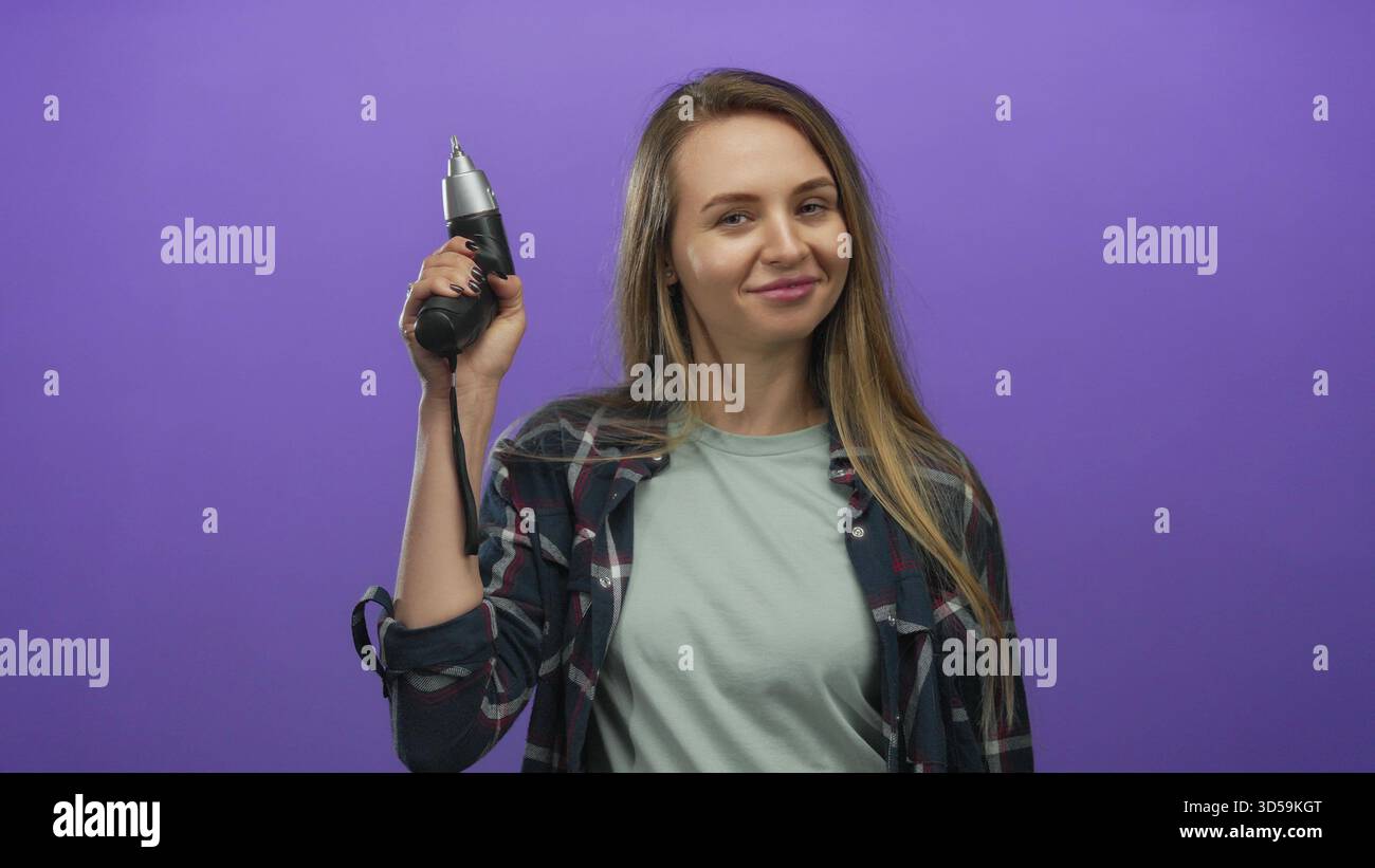 Donna che tiene un trapano di potere con sicurezza davanti a un vivace sfondo viola, che mostra indipendenza, empowerment e moderno spirito fai da te. Foto Stock