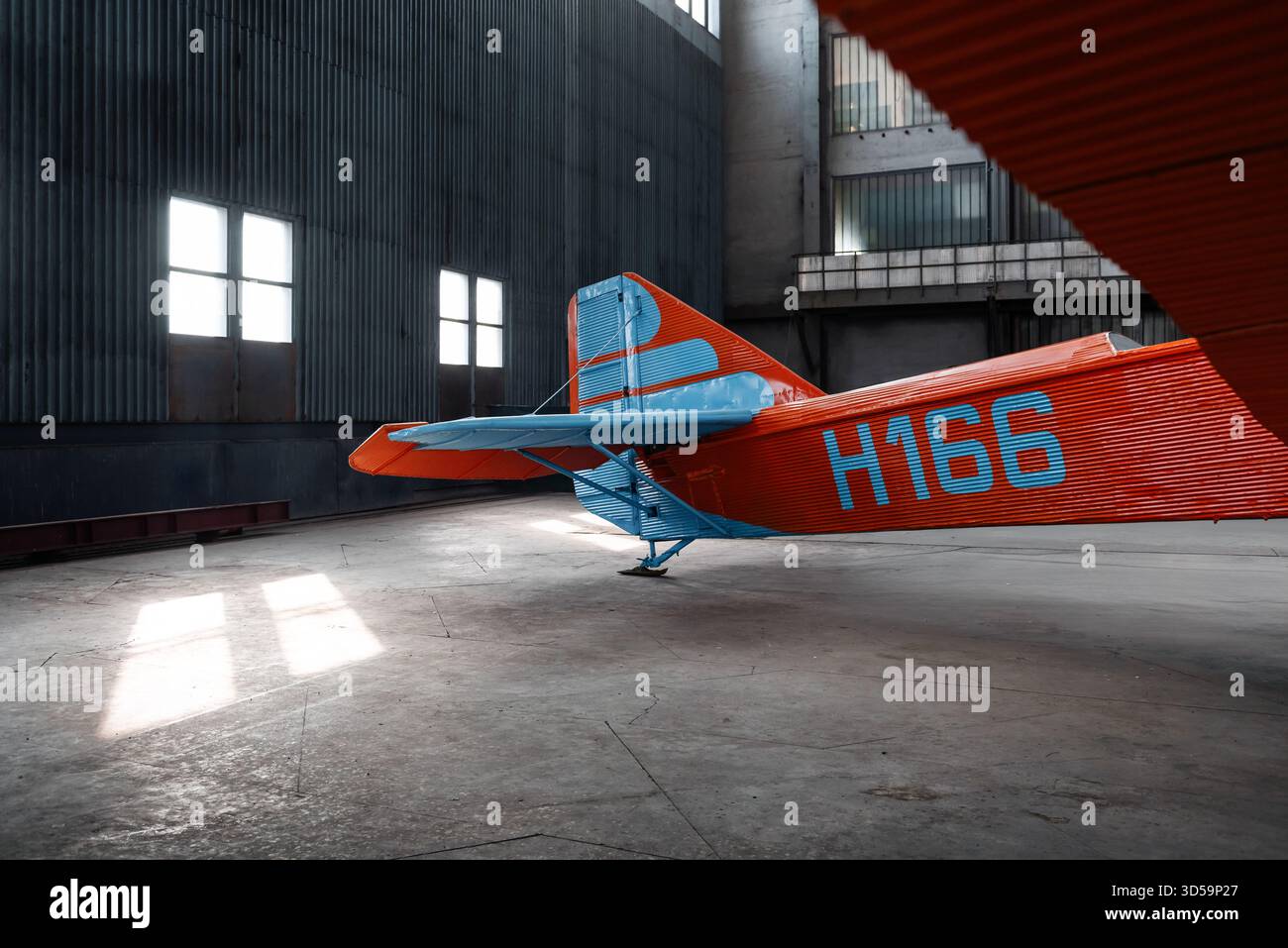 Vecchio aereo ANT-7 anni '1930 in un ampio hangar con grandi finestre. Empennage di storico aereo rosso con strisce blu sul timone e stabilizzatore verticale. Foto Stock