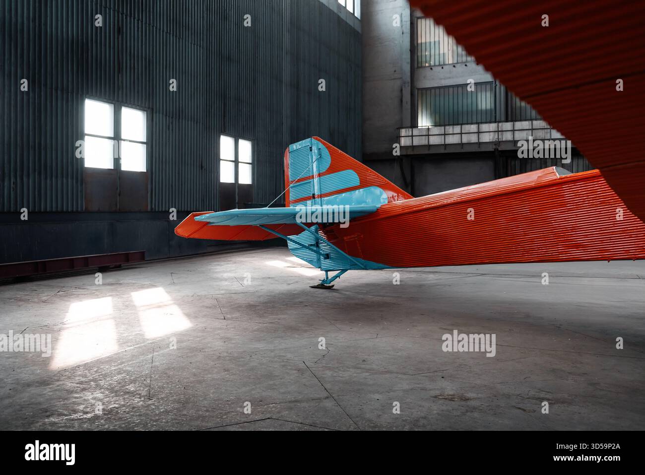 La coda di un vecchio aereo in un ampio hangar con grandi finestre. Empennage di aereo rosso con strisce blu sul timone e stabilizzatore verticale. Foto Stock