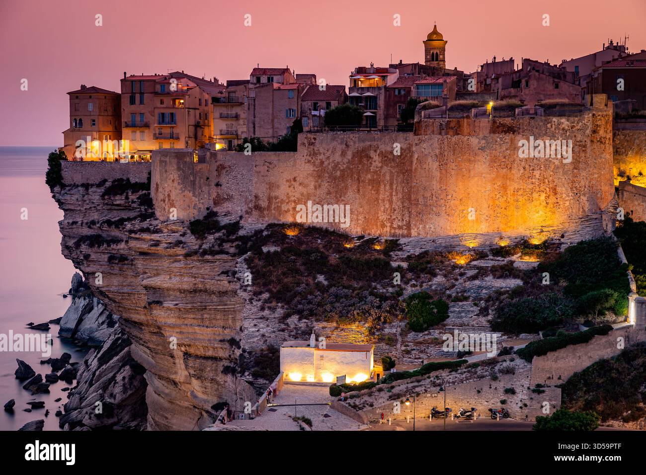 Un tramonto spettacolare bagna una fortezza medievale sulla scogliera e una vivace cittadina costiera in una luce calda, Corsica, Francia Foto Stock