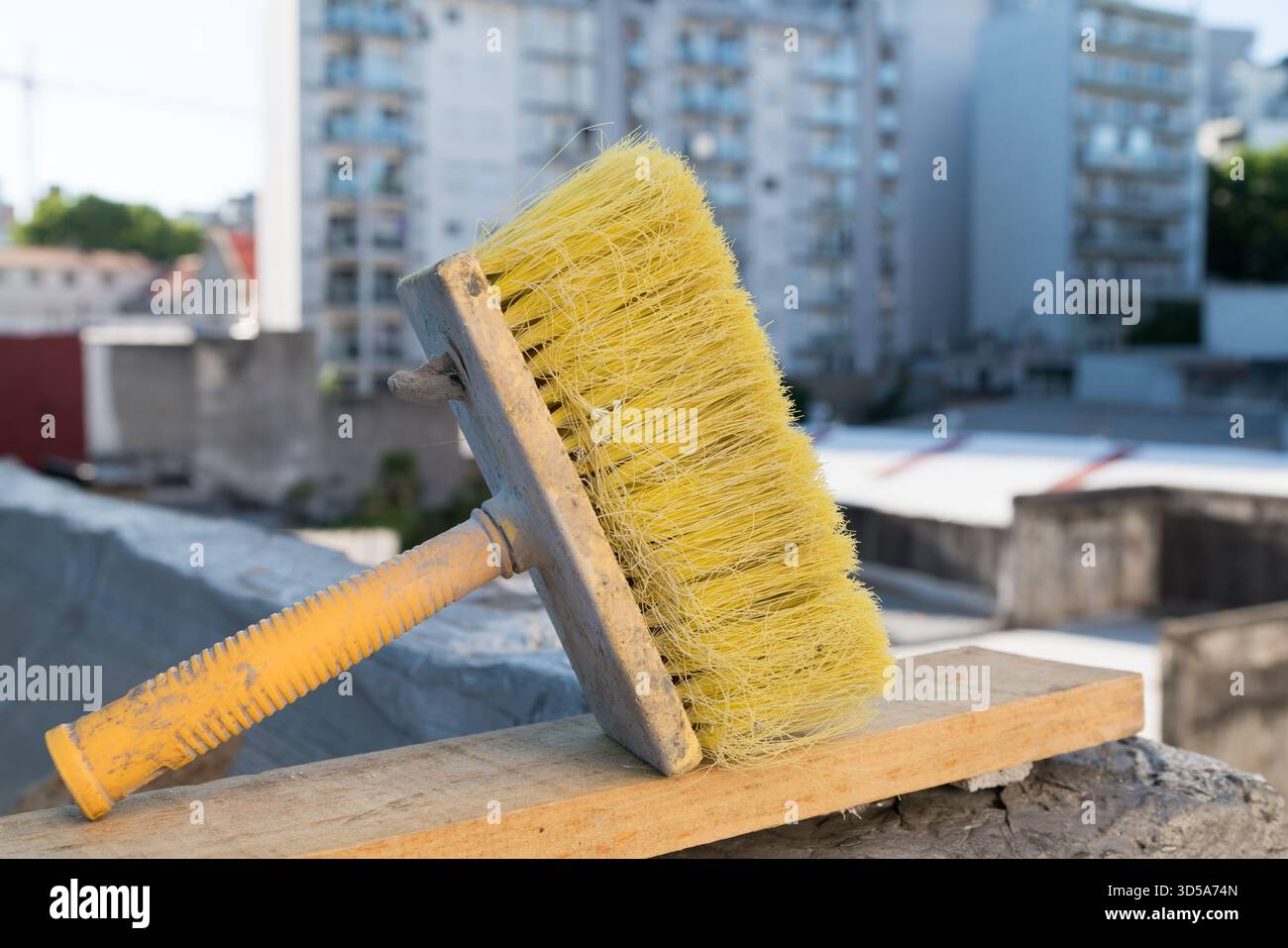 spazzolina gialla usurata su una tavola di legno con vista sulla città Foto Stock