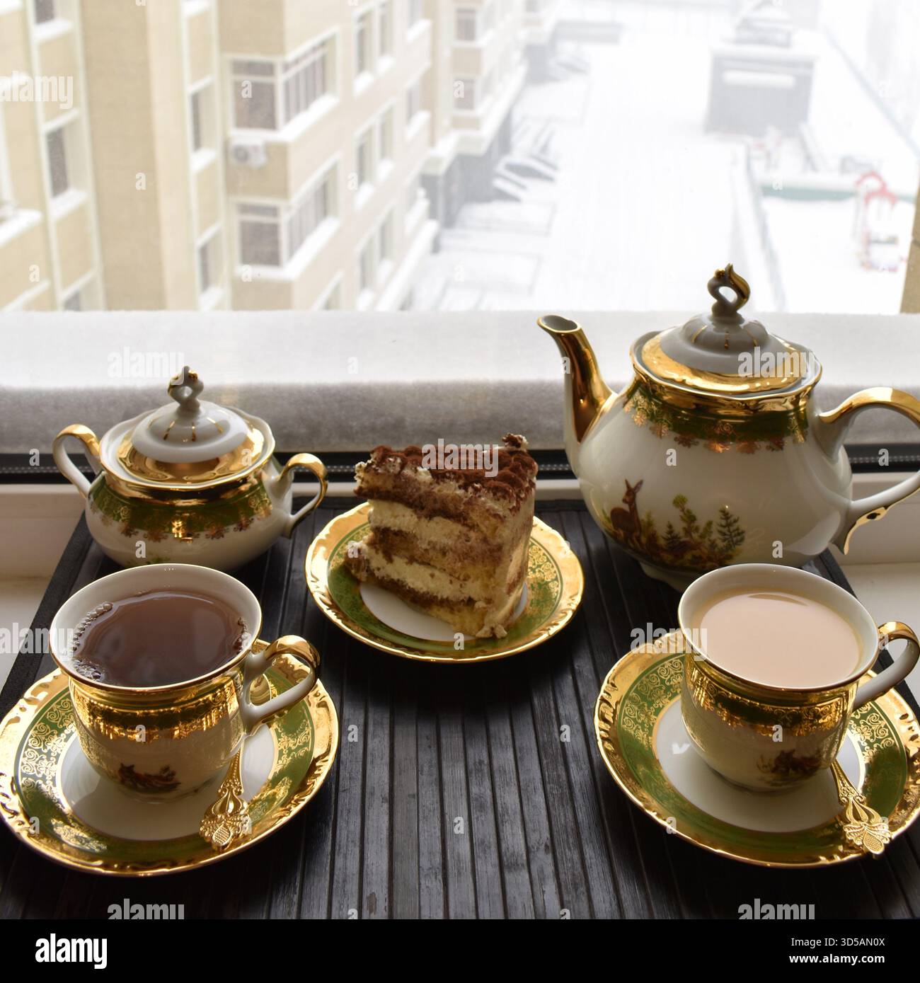 Tè e torta in un lussuoso set da tè per due davanti alla finestra con vista sul cortile innevato. Foto Stock