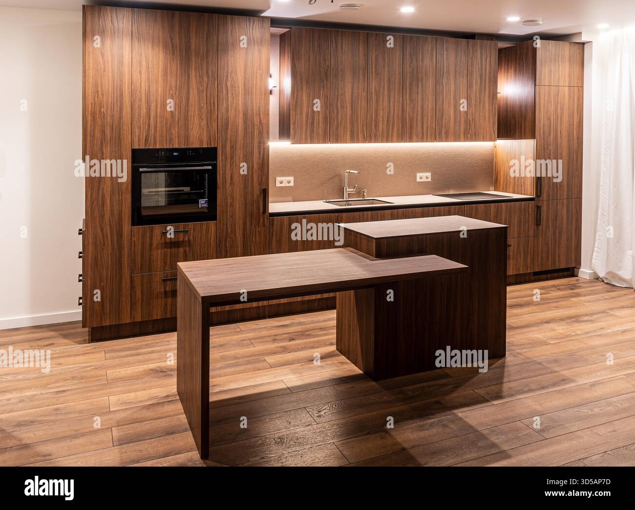 Gli interni moderni della cucina sono dotati di armadi in legno, elettrodomestici integrati e una calda illuminazione ambiente che mette in risalto un design minimalista Foto Stock
