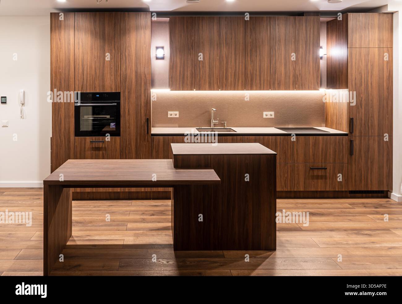 Gli interni moderni della cucina sono dotati di armadi in legno, elettrodomestici integrati e una calda illuminazione ambiente che mette in risalto un design minimalista Foto Stock