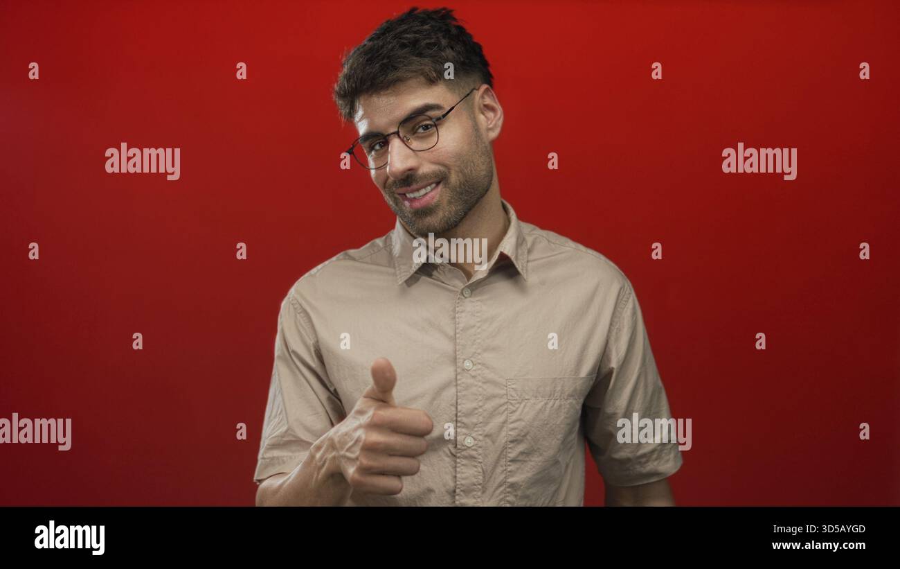 Uomo che indossa camicia e occhiali beige con gesti di palme aperte e un sorriso sottile in studio rosso; curiosità. Foto Stock