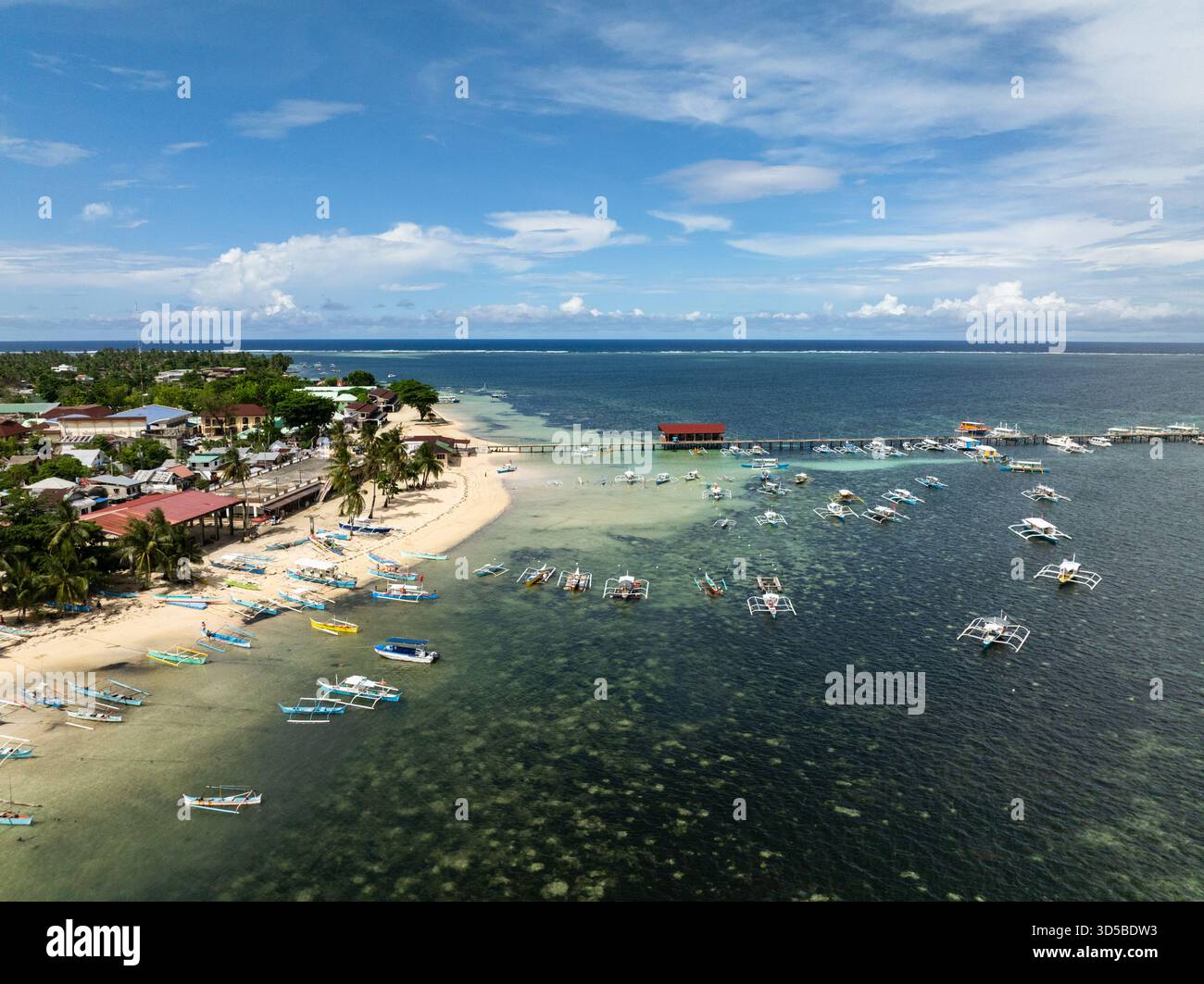 Barche da pesca ancorate vicino al molo con insediamento costiero e litorale sabbioso. Generale Luna, Siargao, Filippine. Foto Stock