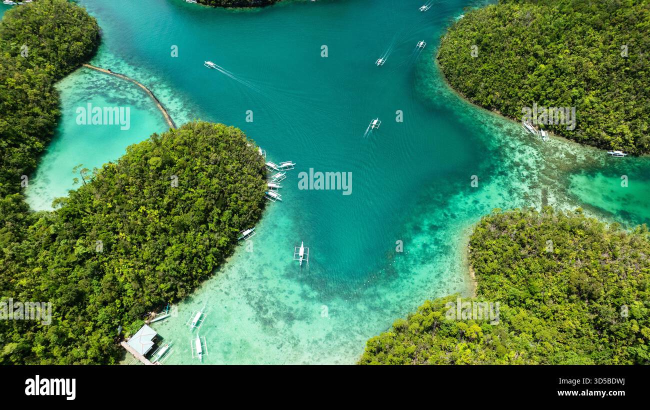 Mare poco profondo con barriera corallina e barche tra le isole della foresta verde sotto la luce intensa. Siargao, Filippine. Laguna blu di Sugba. Foto Stock
