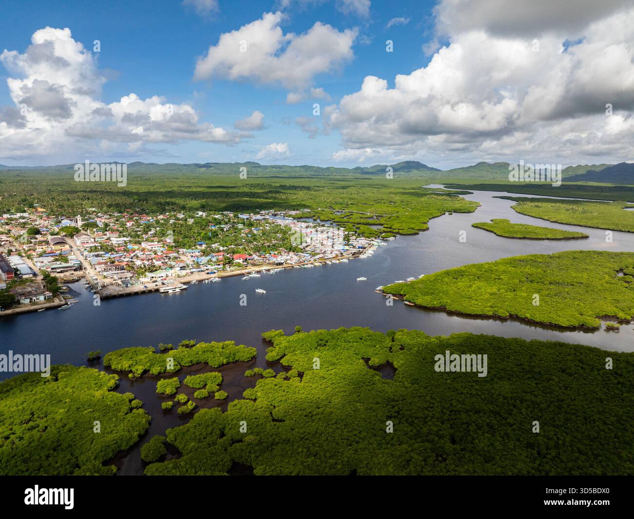 Città lungo le rive del fiume circondata da foreste di mangrovie e montagne sullo sfondo. Siargao, Filippine. Foto Stock