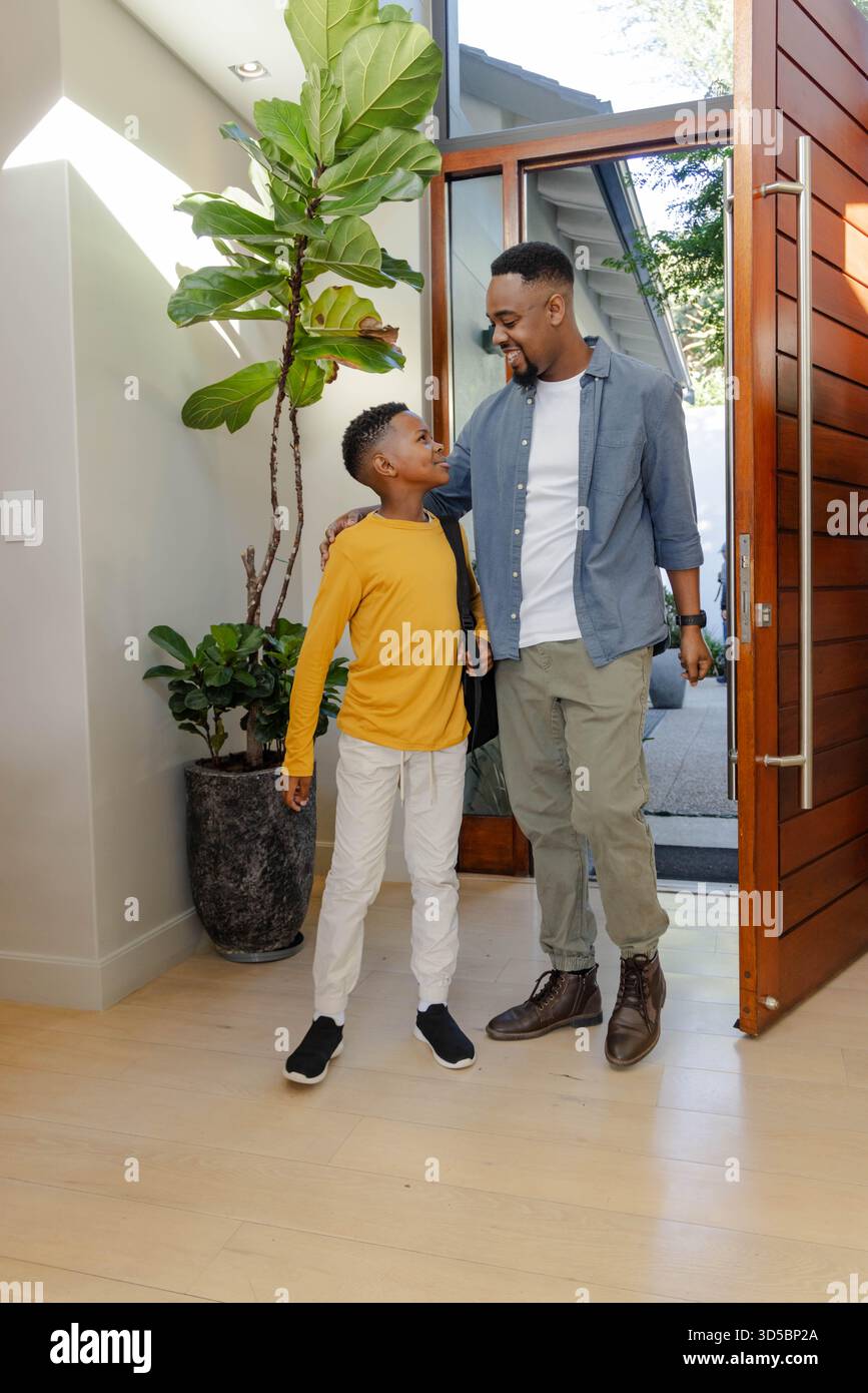 Padre e figlio sorridono e legano a casa vicino alla porta d'ingresso aperta Foto Stock