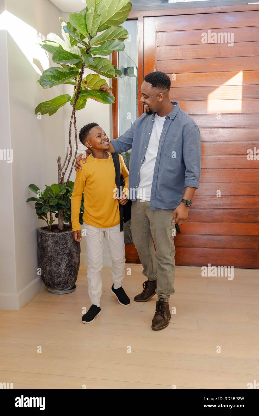 Padre e figlio sorridono, si preparano per la scuola, in piedi vicino alla porta d'ingresso Foto Stock