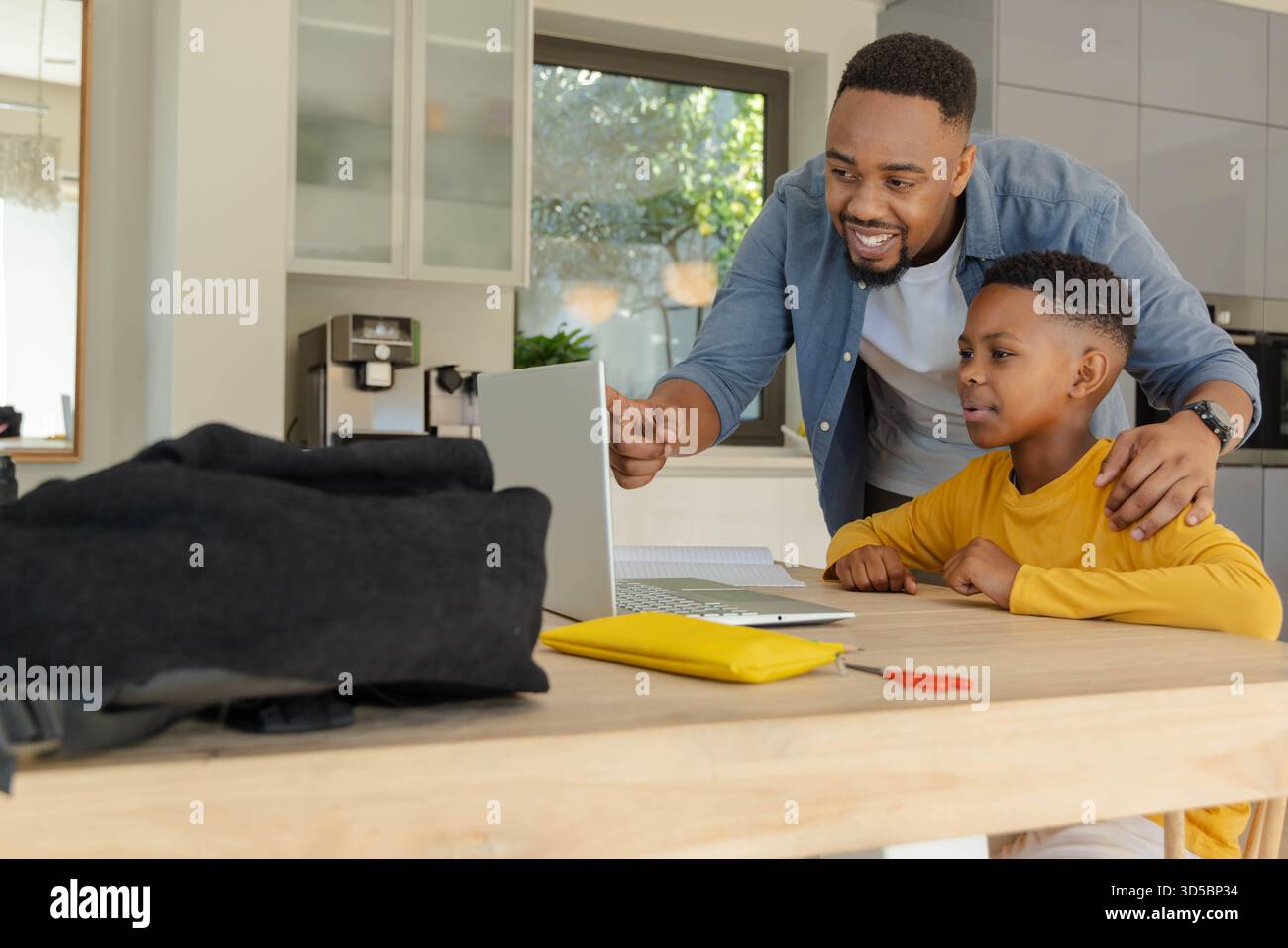 Padre e figlio che usano un computer portatile a casa, imparano insieme con i sorrisi Foto Stock