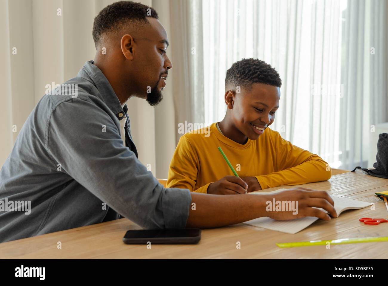 Padre che aiuta il figlio con i compiti a casa, sorridente e impegnato nell'apprendimento Foto Stock