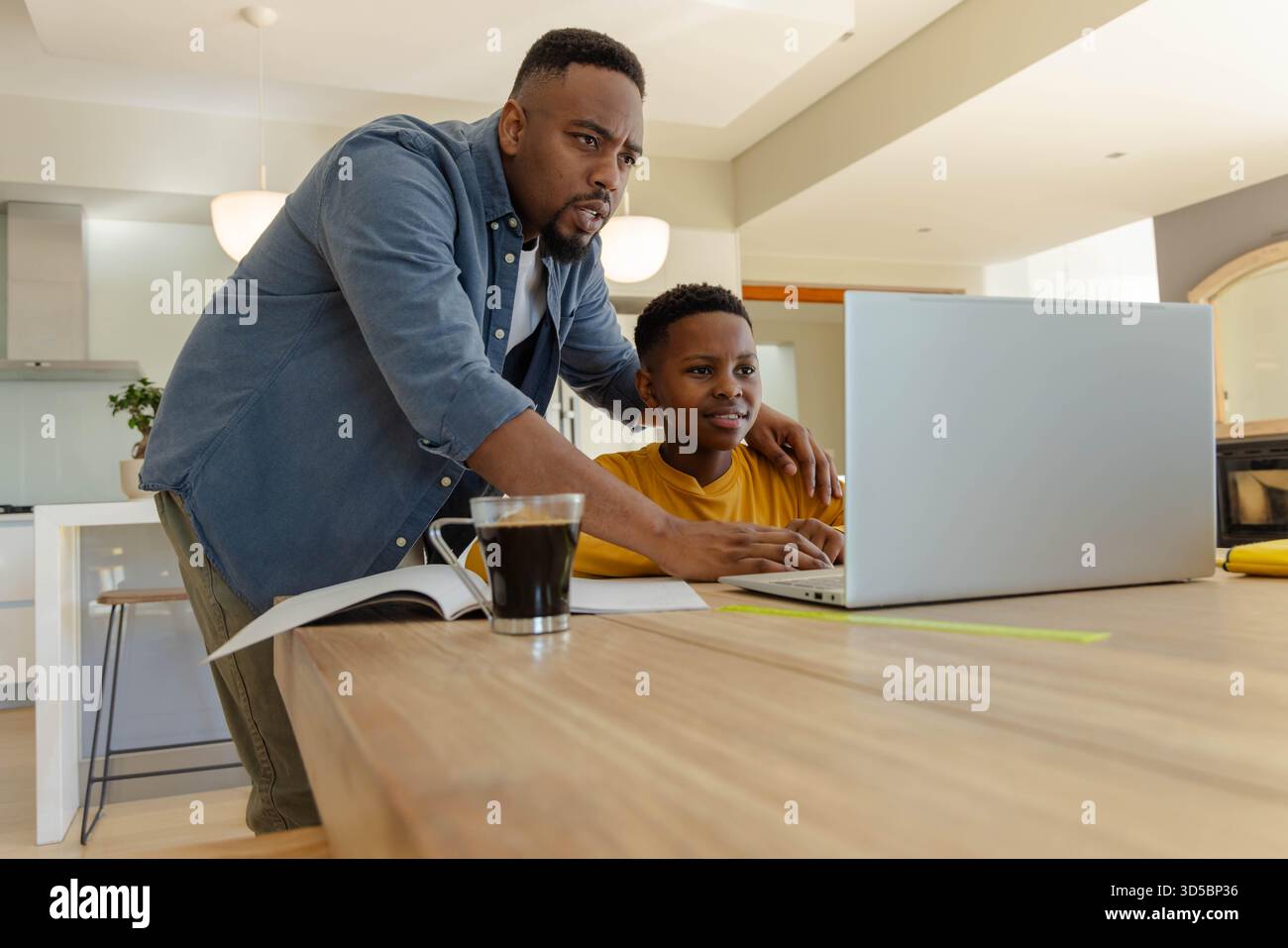 Padre che guida il figlio che utilizza un notebook a casa, entrambi concentrati sull'apprendimento insieme Foto Stock