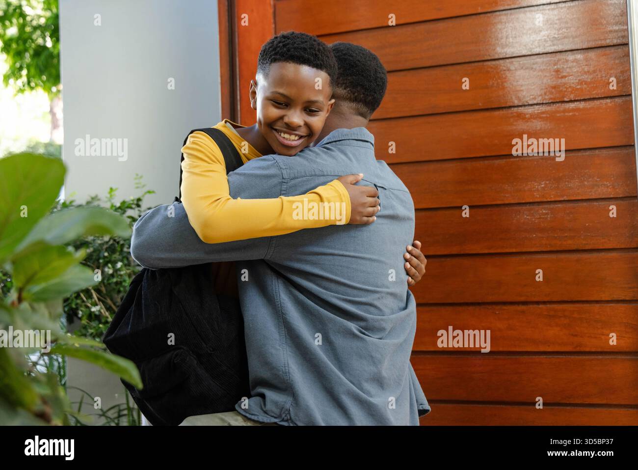 Padre e figlio afroamericani che mostrano tecnica di rasatura nel bagno di casa con parete di legno Foto Stock