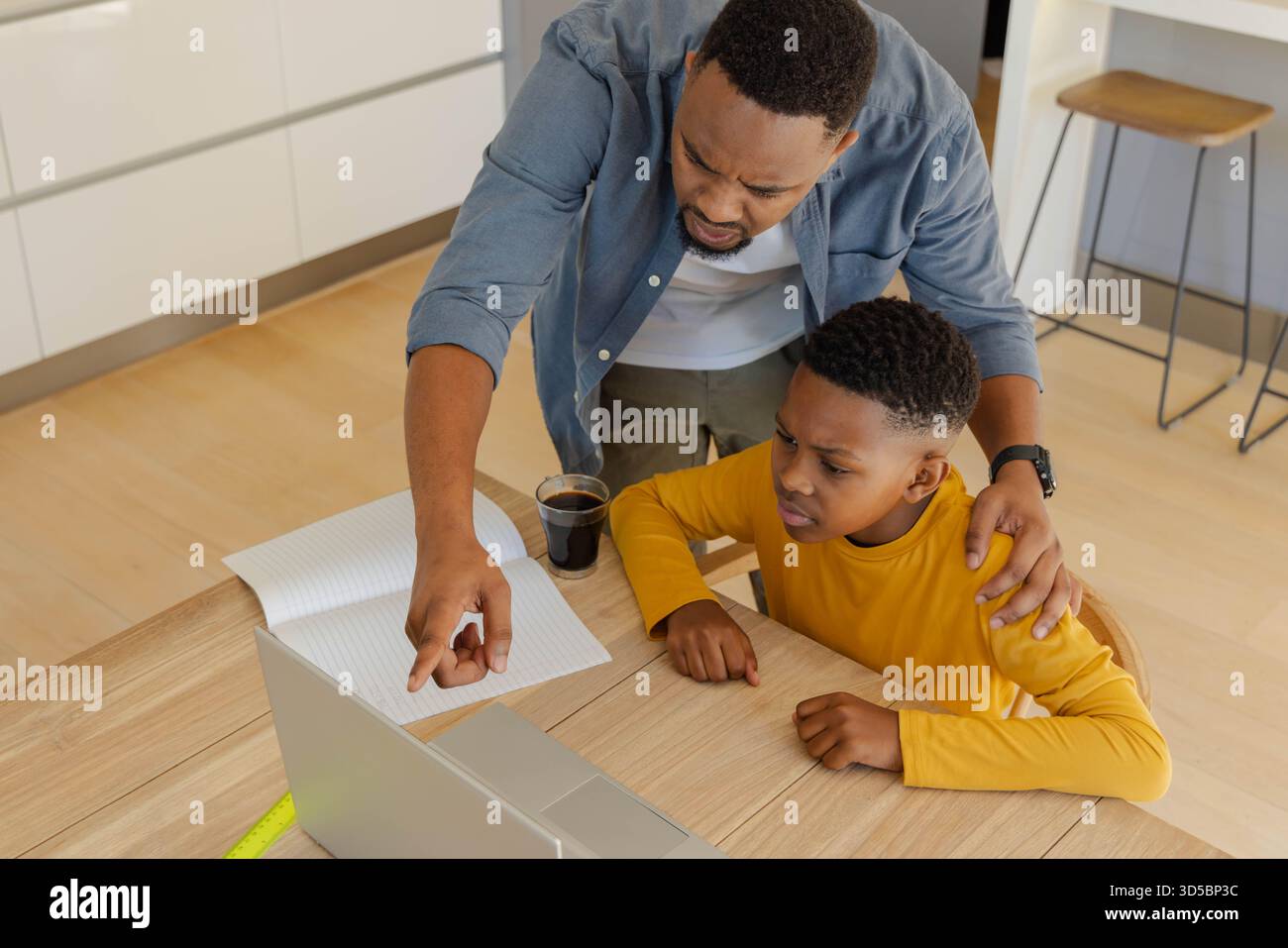 Padre che aiuta il figlio con i compiti sul notebook a casa, puntando sullo schermo Foto Stock
