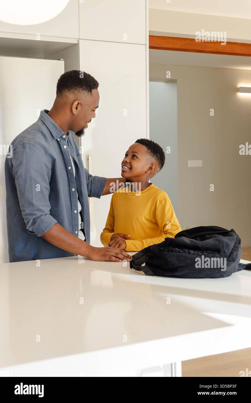 Padre e figlio afroamericani che parlano in cucina con lo zaino sul bancone Foto Stock