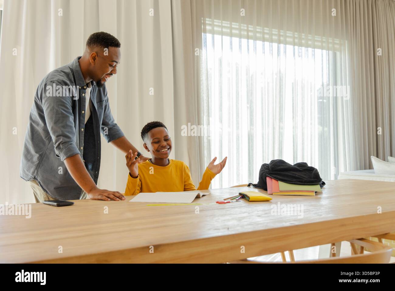 Padre che aiuta il figlio con i compiti a casa, sorridendo e divertendosi insieme Foto Stock