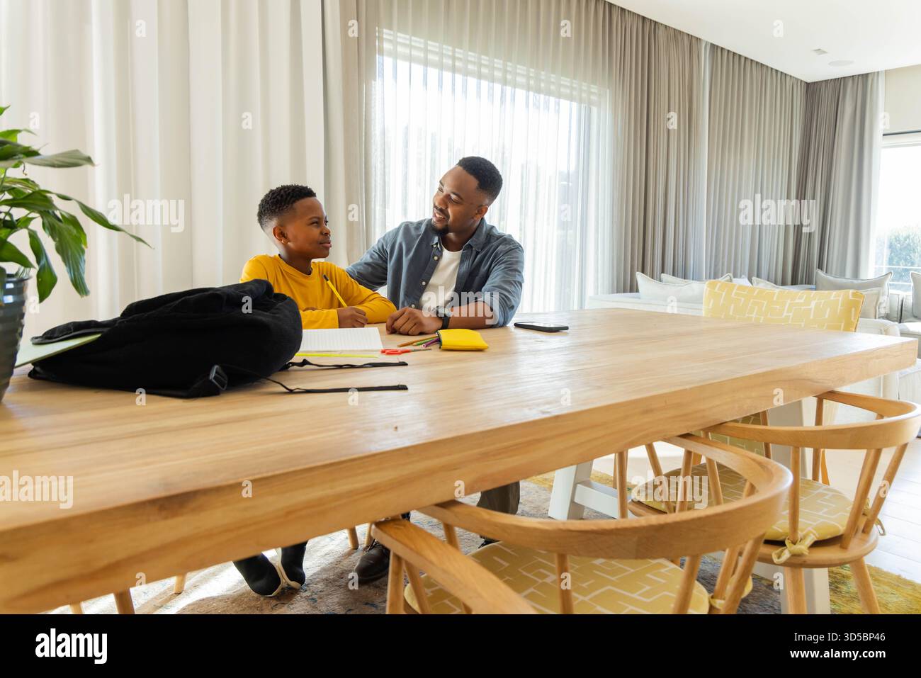 Padre e figlio fanno i compiti insieme a casa, sorridono e legano Foto Stock