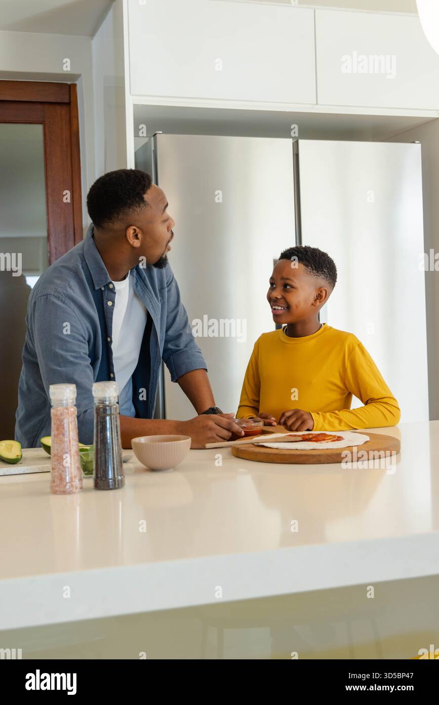 Padre e figlio preparano il pasto insieme nella cucina moderna, condividendo momenti di gioia Foto Stock