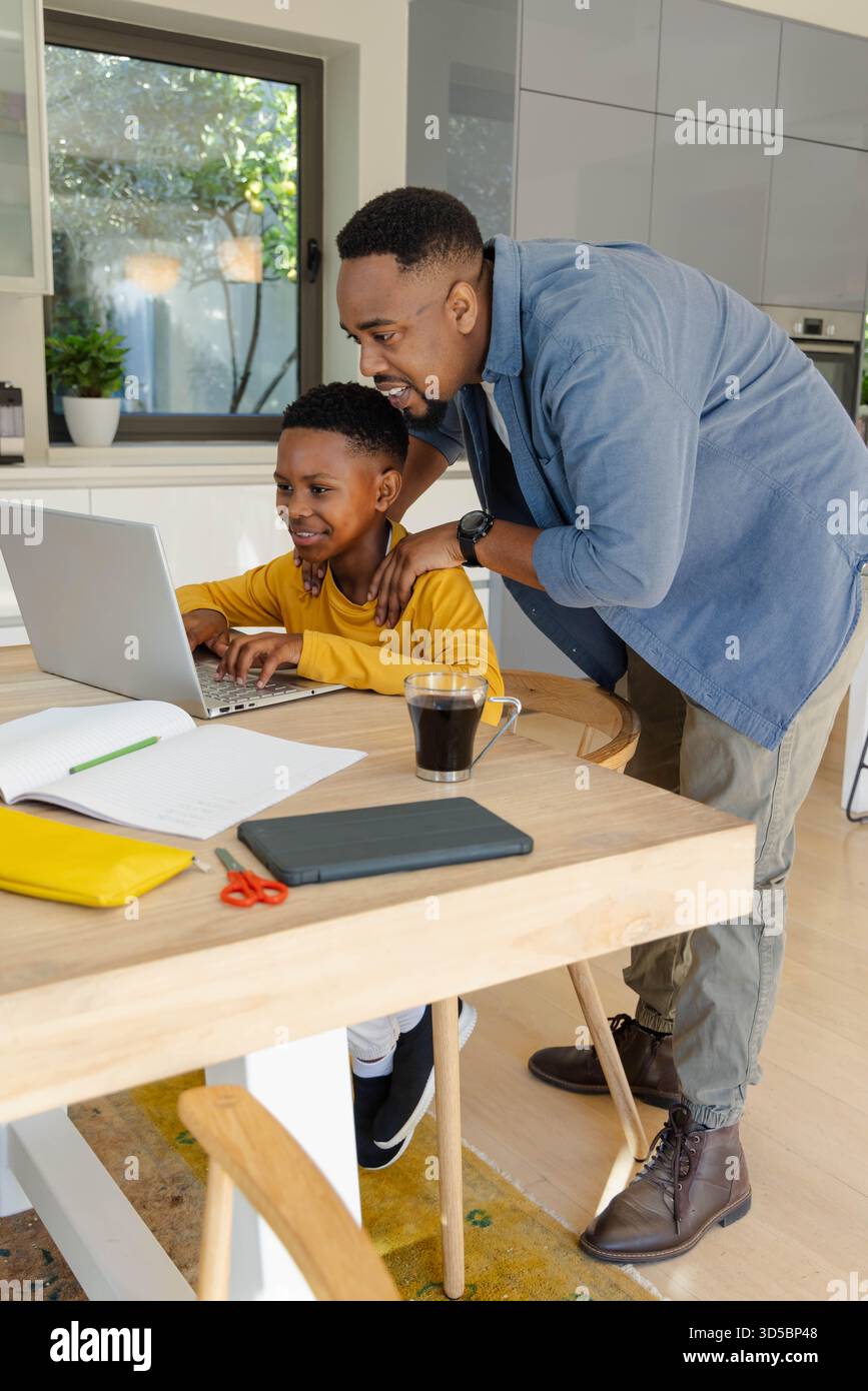 Padre afroamericano che aiuta il figlio con i compiti sul computer portatile al tavolo della cucina Foto Stock