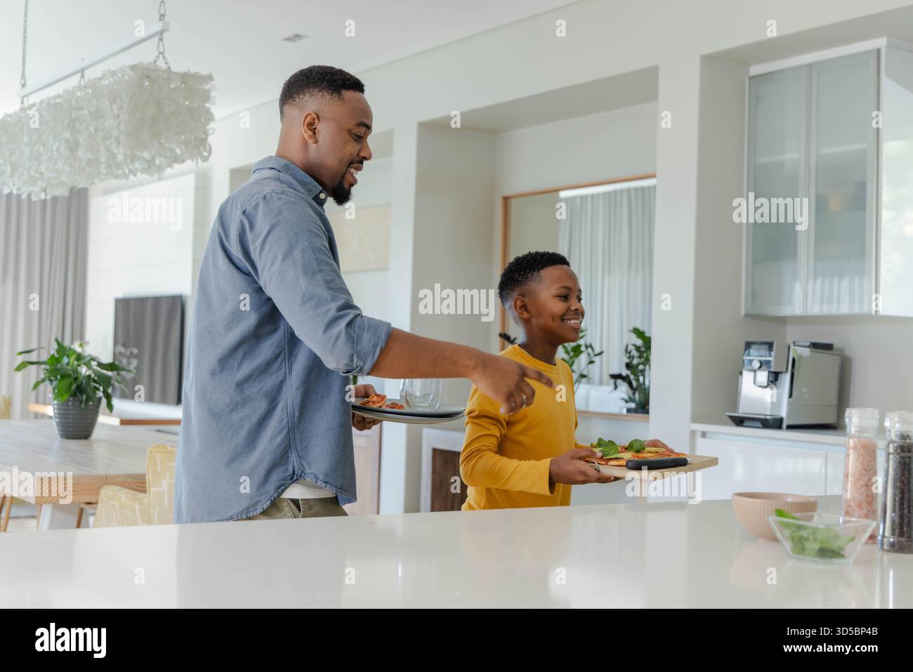 Padre e figlio afroamericani preparano la colazione insieme in una cucina moderna, sorridenti e leganti Foto Stock