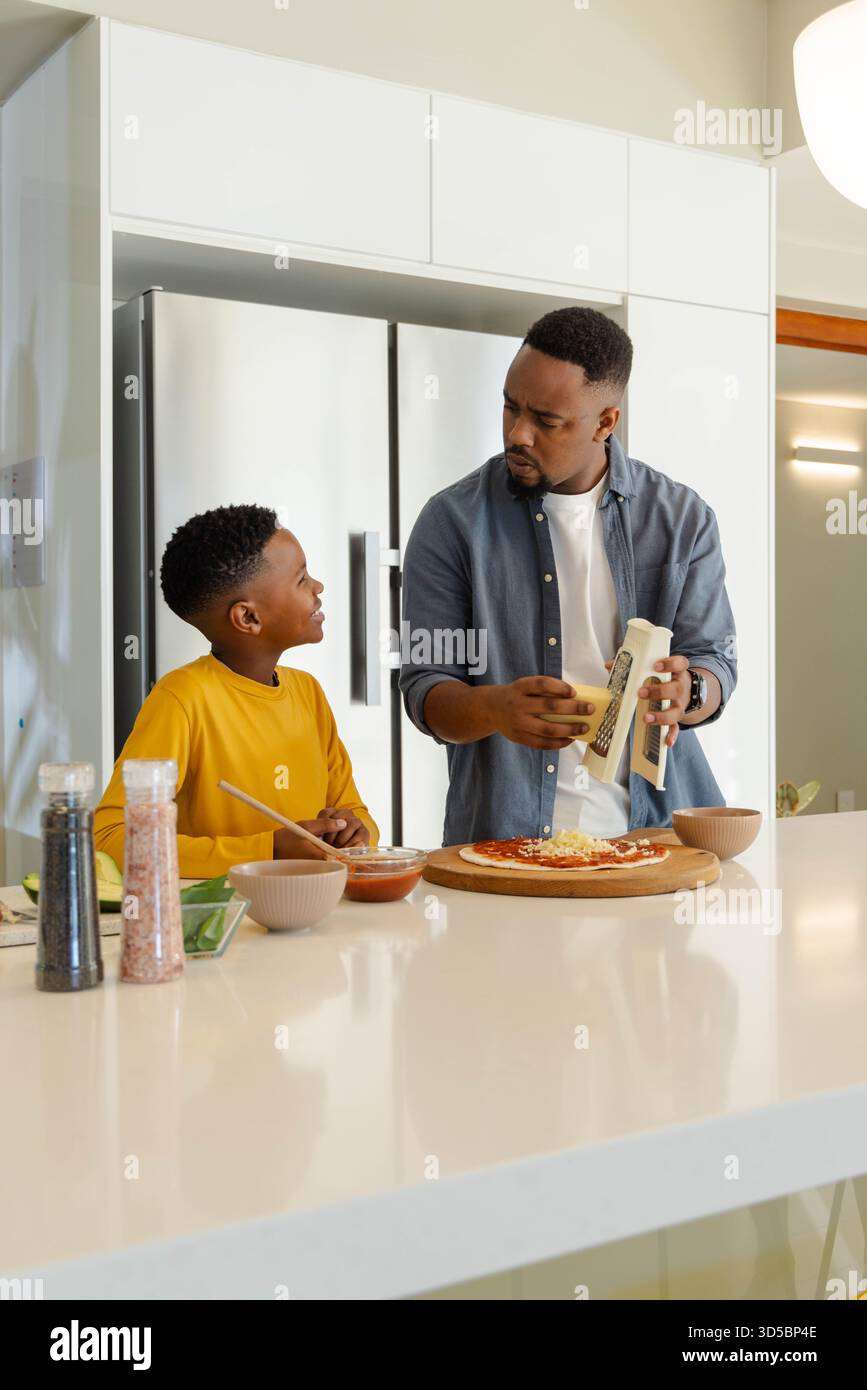In cucina, padre e figlio preparano la pizza fatta in casa, trascorrendo del tempo di legame di qualità Foto Stock