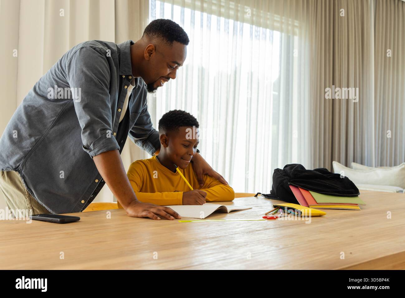 Padre che aiuta il figlio con i compiti a casa, sorridente e fidanzato Foto Stock