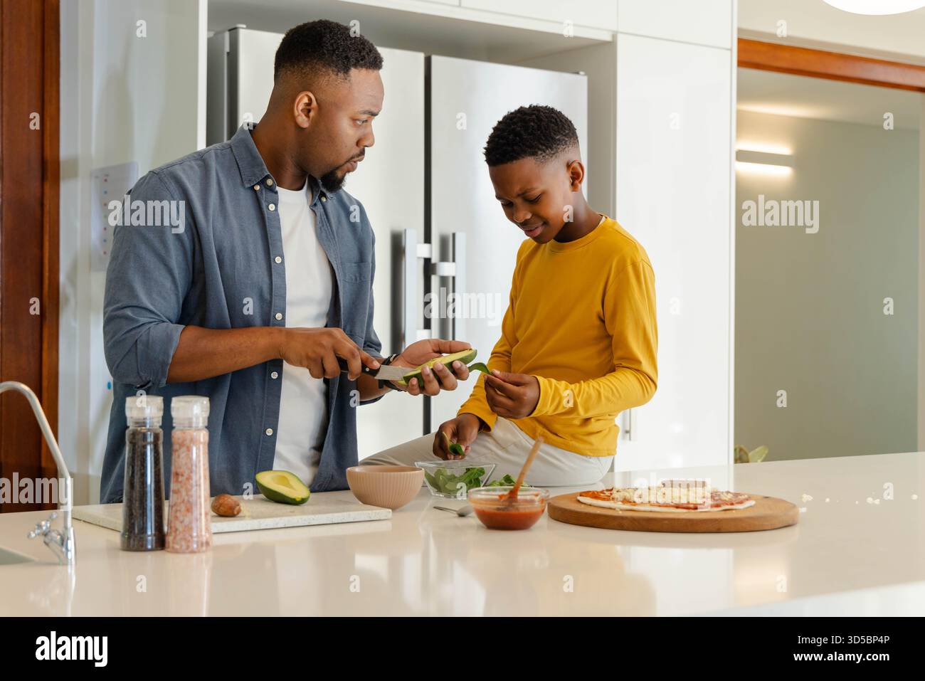 Padre e figlio preparano insieme pasti sani in cucina moderna, legando felicemente Foto Stock