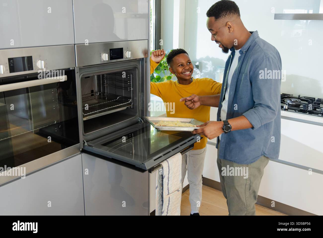 Padre e figlio cucinano insieme in una cucina moderna, godendo del tempo di qualità Foto Stock