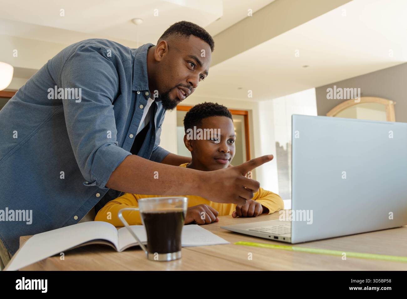 Padre che guida il figlio sul laptop a casa, concentrandosi sull'apprendimento insieme Foto Stock