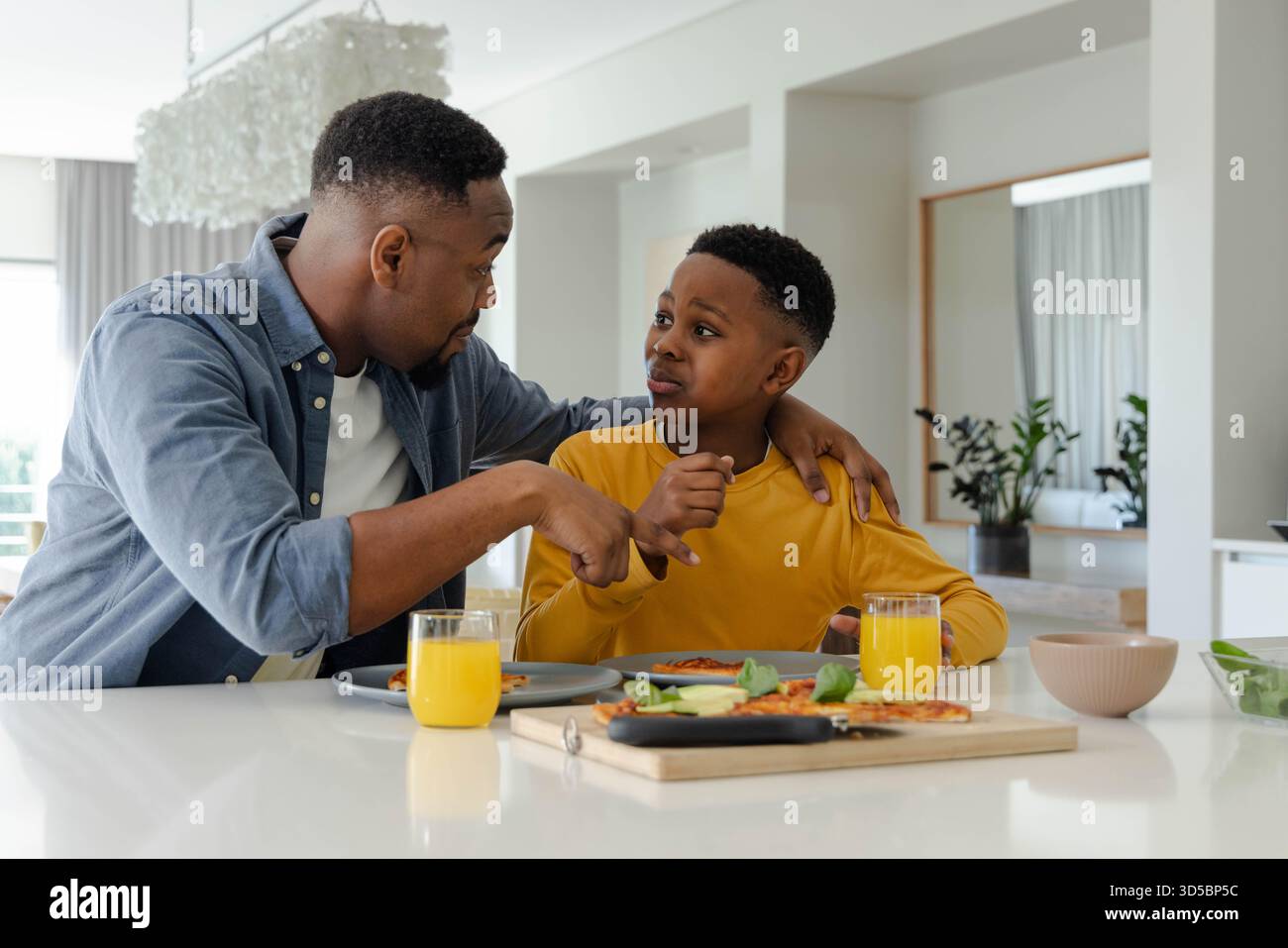 Padre e figlio afroamericani si godono la colazione insieme, condividendo conversazione nella cucina di casa Foto Stock