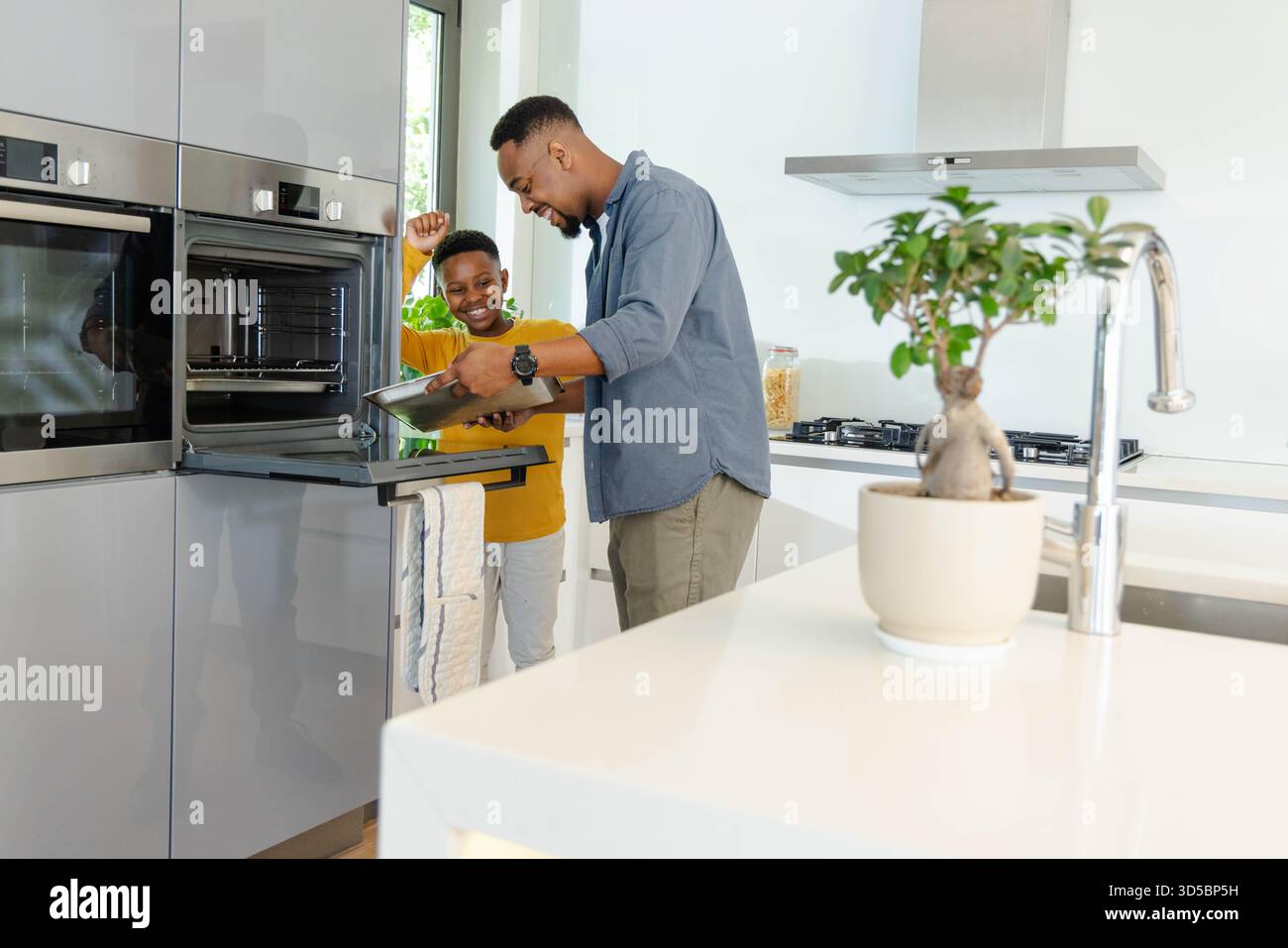 Padre e figlio cucinano insieme in una cucina moderna, godendo del tempo di qualità Foto Stock