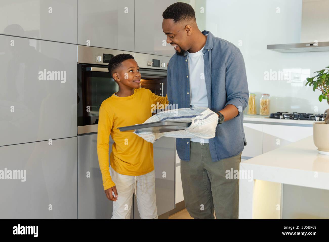 Padre e figlio cucinano insieme nella cucina moderna, condividendo momenti di gioia Foto Stock