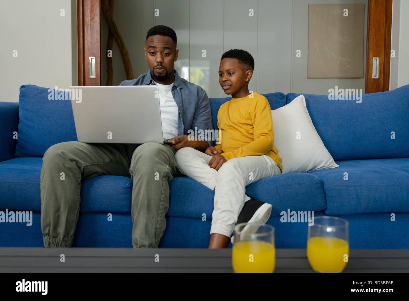 Padre e figlio afroamericani seduti sul divano con un computer portatile, godendo del tempo di qualità insieme Foto Stock