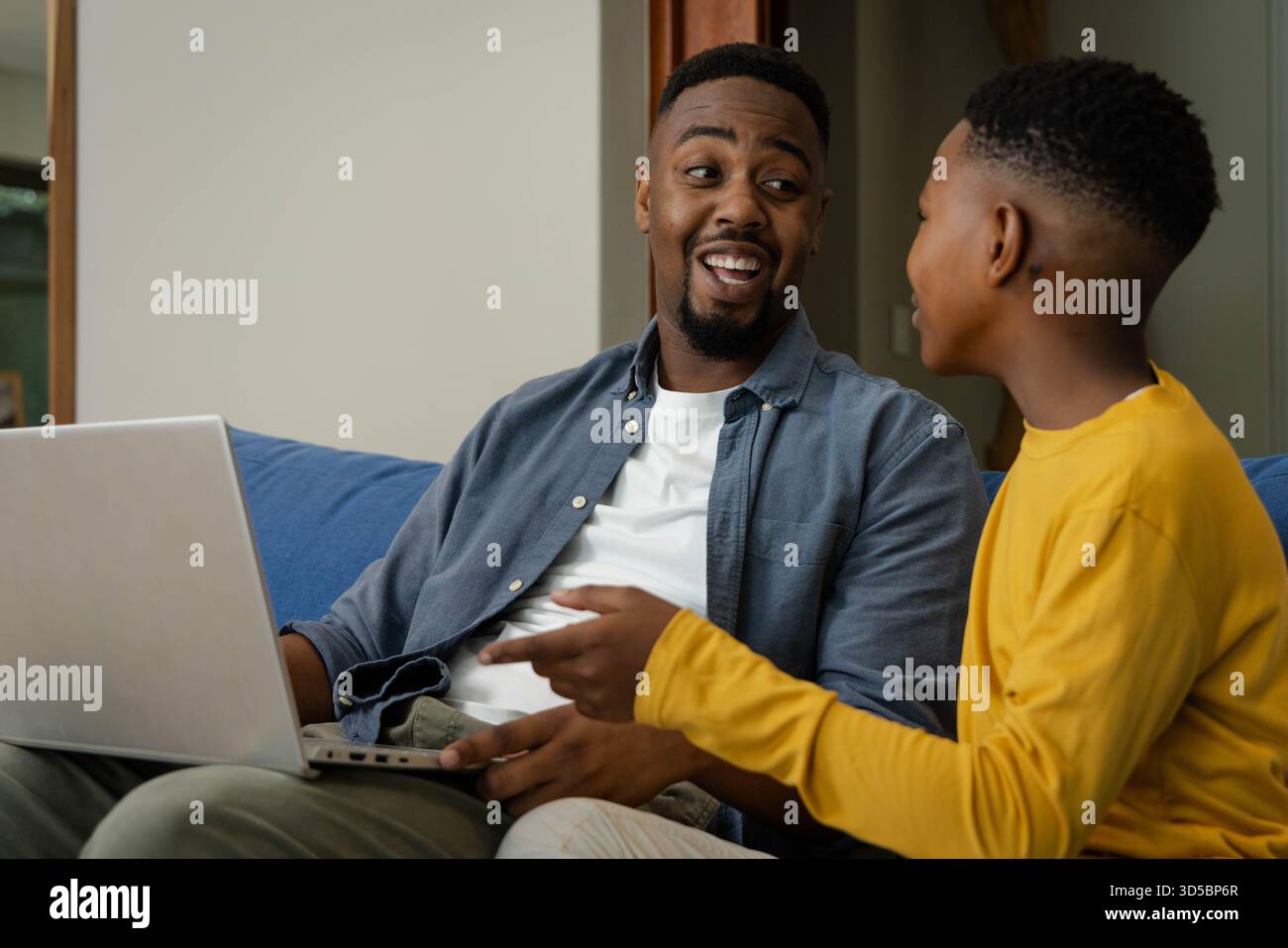 Padre e figlio afroamericani si legano a casa, sorridono e usano il laptop insieme sul divano Foto Stock