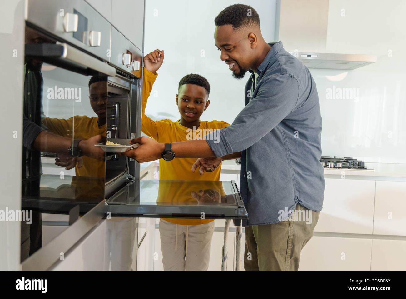 Padre e figlio cucinano insieme in una cucina moderna, godendo del tempo di qualità Foto Stock