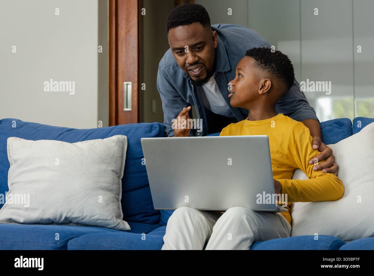 Padre afroamericano che aiuta il figlio a fare i compiti con un portatile a casa, condividendo consigli Foto Stock