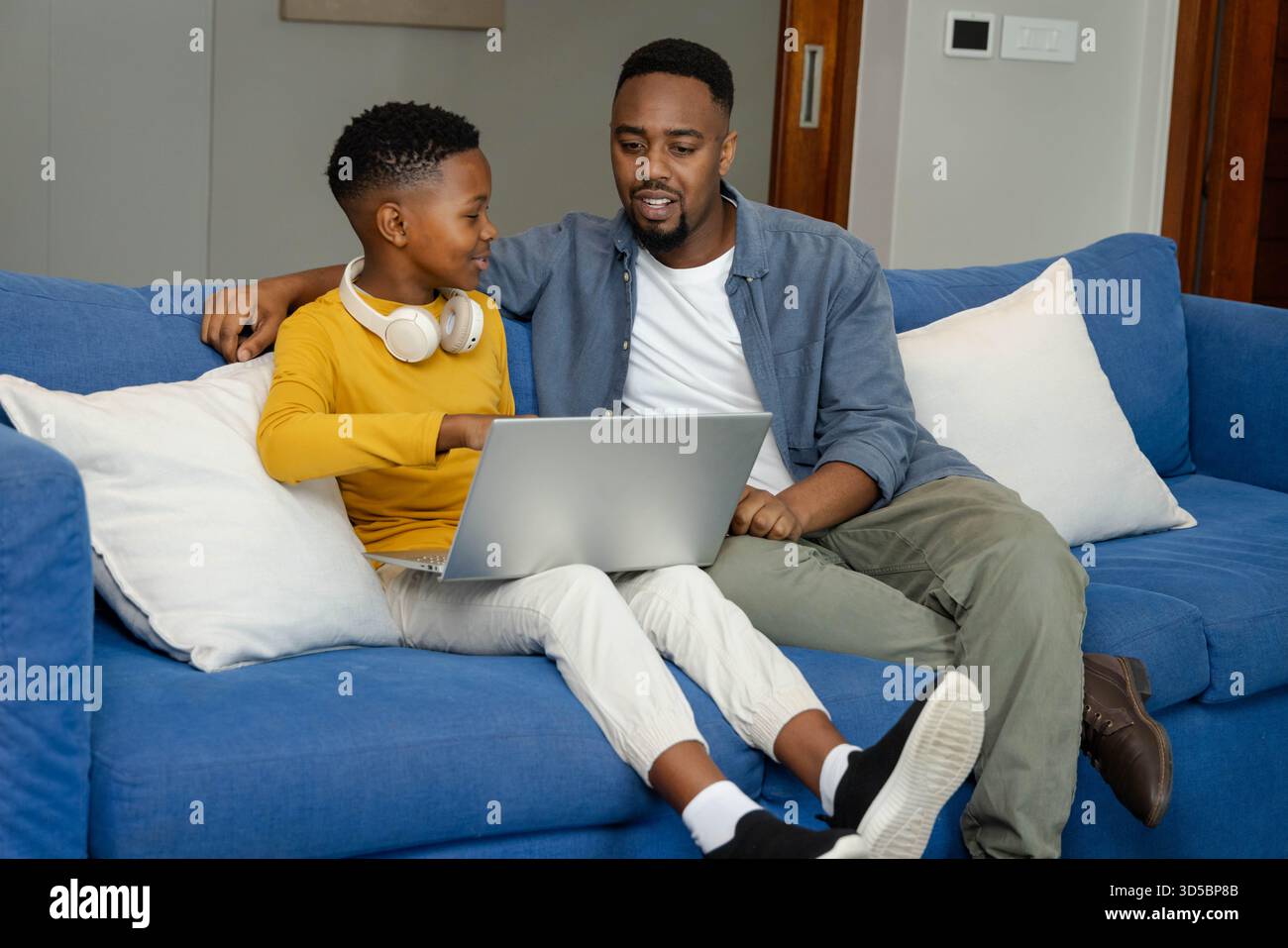 Padre e figlio afroamericani che usano il laptop sul divano, legano e imparano insieme a casa Foto Stock