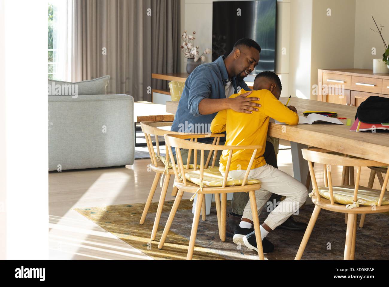 Padre e ragazzo afroamericani che aiutano a studiare nella moderna sala da pranzo, recensendo libri e materiali Foto Stock
