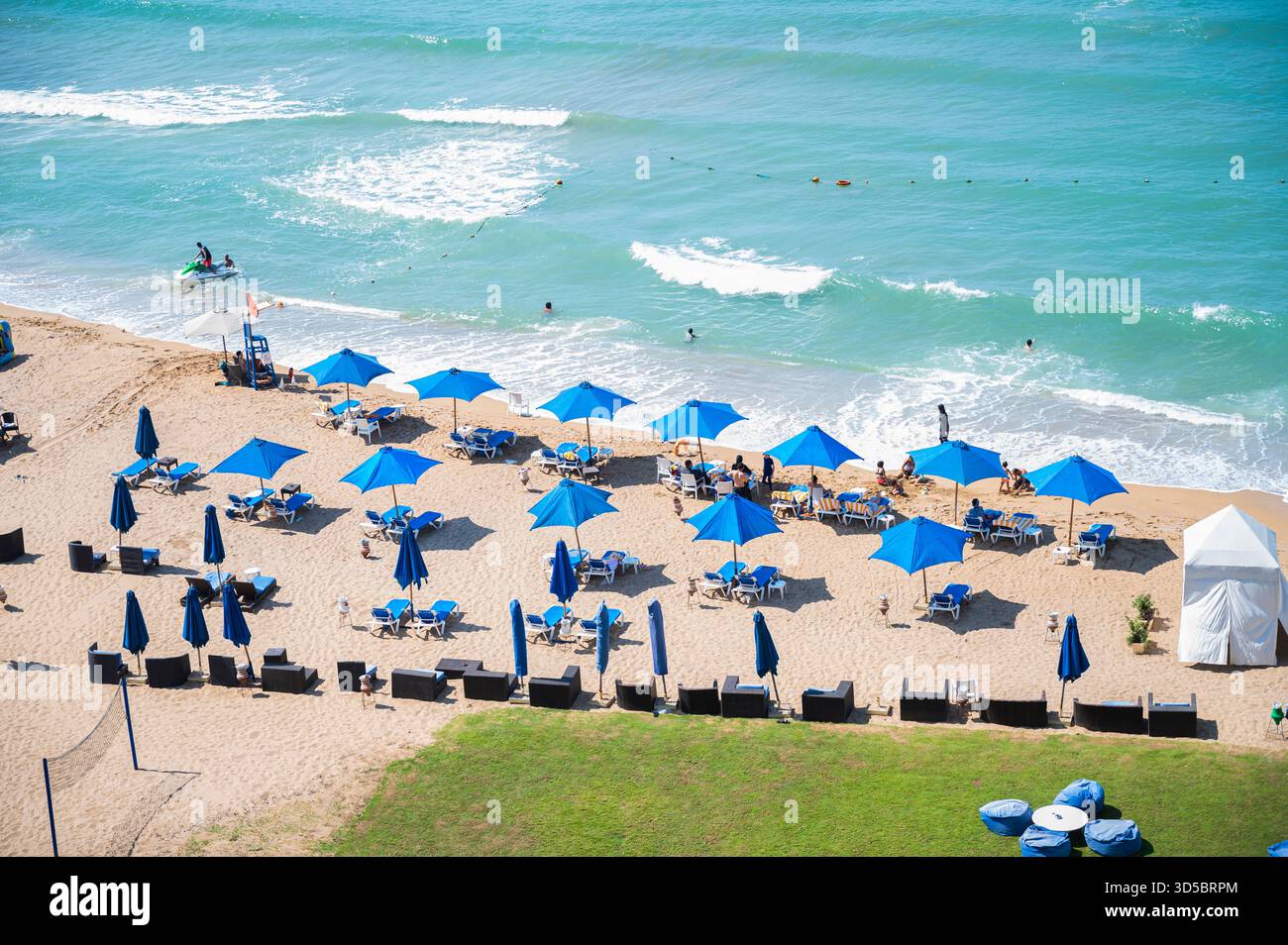 Vista ad alto angolo di una spiaggia dell'Hilton Resort con ombrelloni blu Una fotografia luminosa e ad alto angolo cattura un lussuoso allestimento da resort sulla spiaggia. Foto Stock