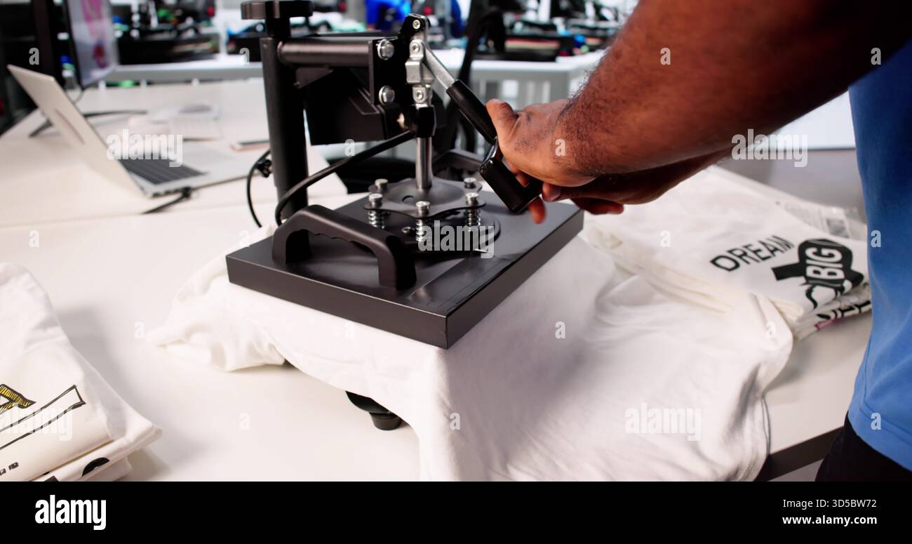 Workshop di stampa di magliette personalizzate: Young Man dimostra la pressa termica Foto Stock