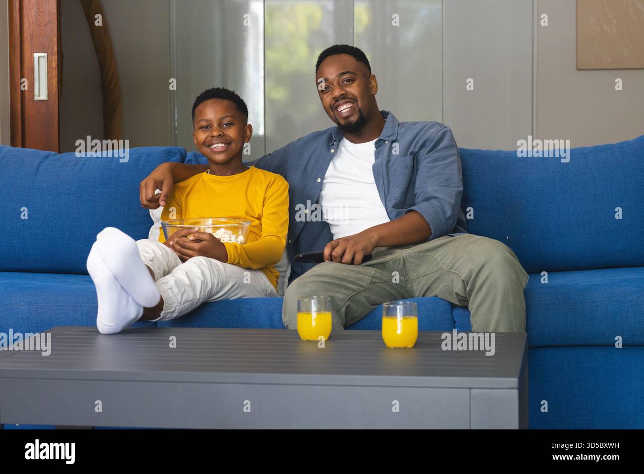 Padre e figlio si godevano la colazione insieme sul divano, sorridendo e legando Foto Stock