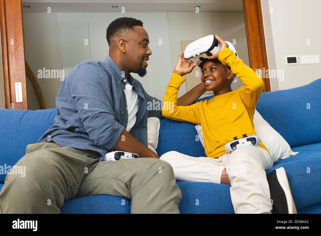 Padre e figlio si divertono a giocare in realtà virtuale insieme sul divano del soggiorno Foto Stock