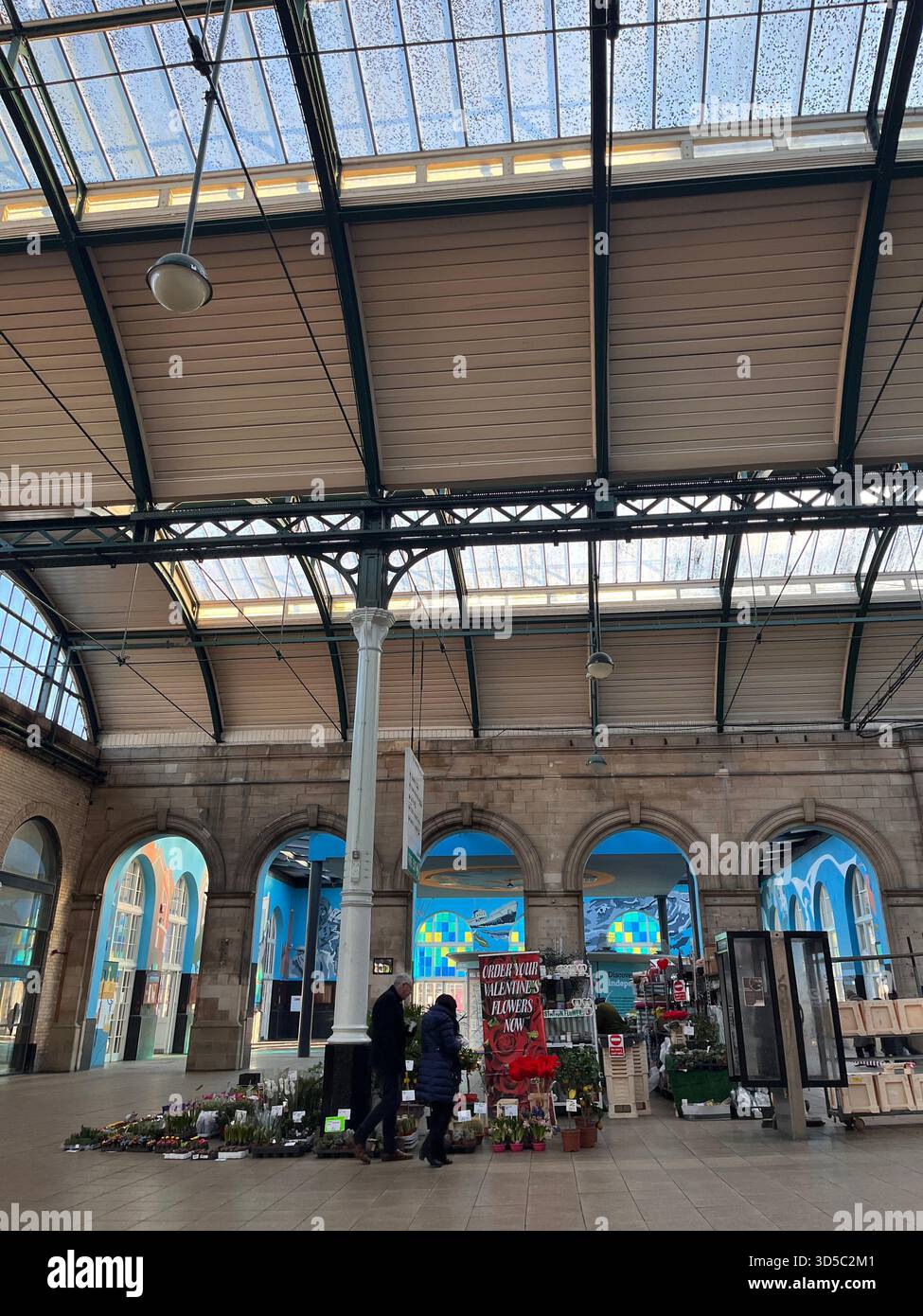 Interno di uno storico mercato vittoriano con colonne in ferro, tetto in vetro, bancarelle di fiori e negozi di persone a Hull, Inghilterra. - Immagine stock catturata con smartphone