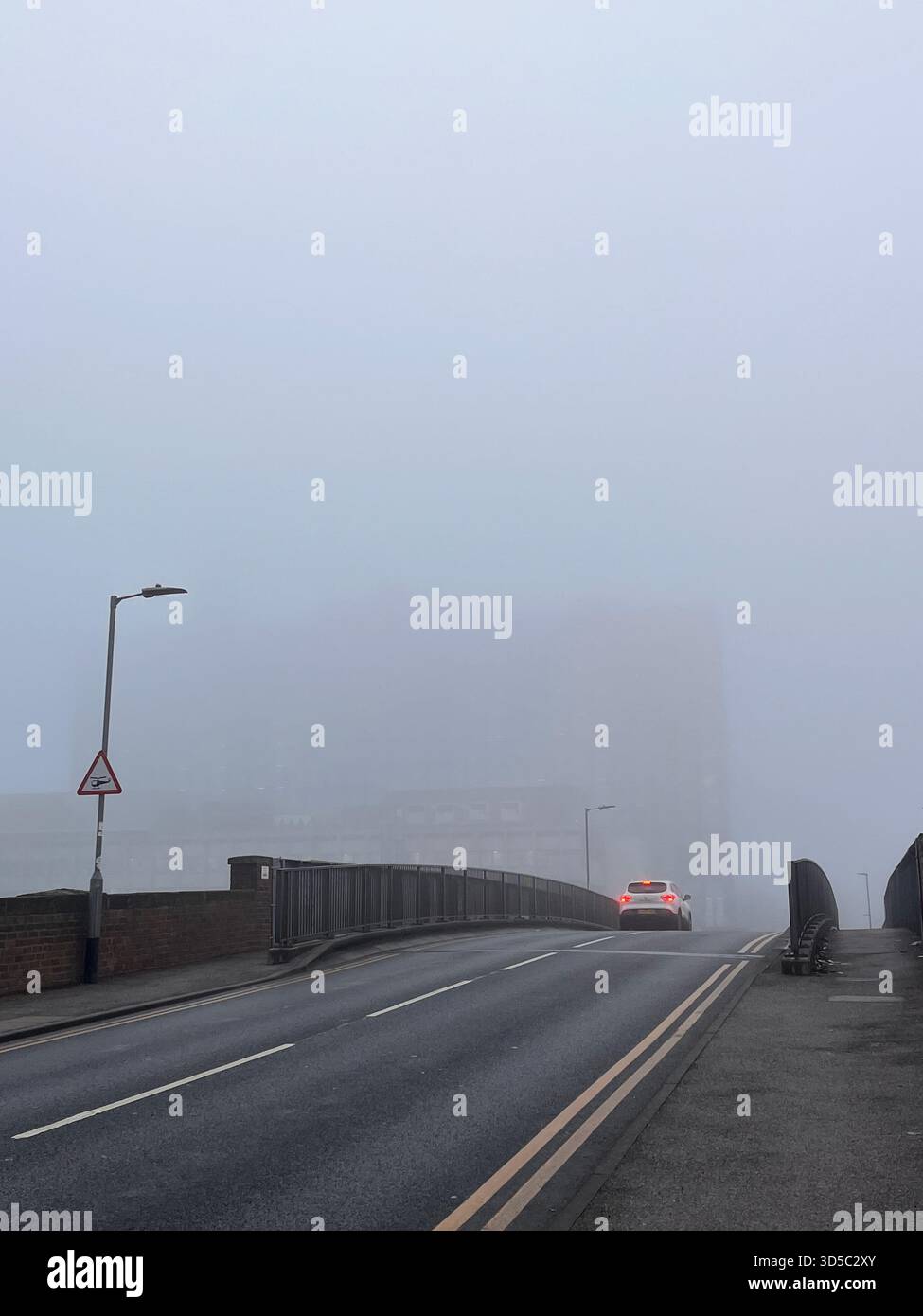 Vista suggestiva di una strada nebbiosa che conduce su un ponte a Hull, Inghilterra. La bassa visibilità e la nebbia creano un ambiente di trasporto invernale tranquillo Foto Stock