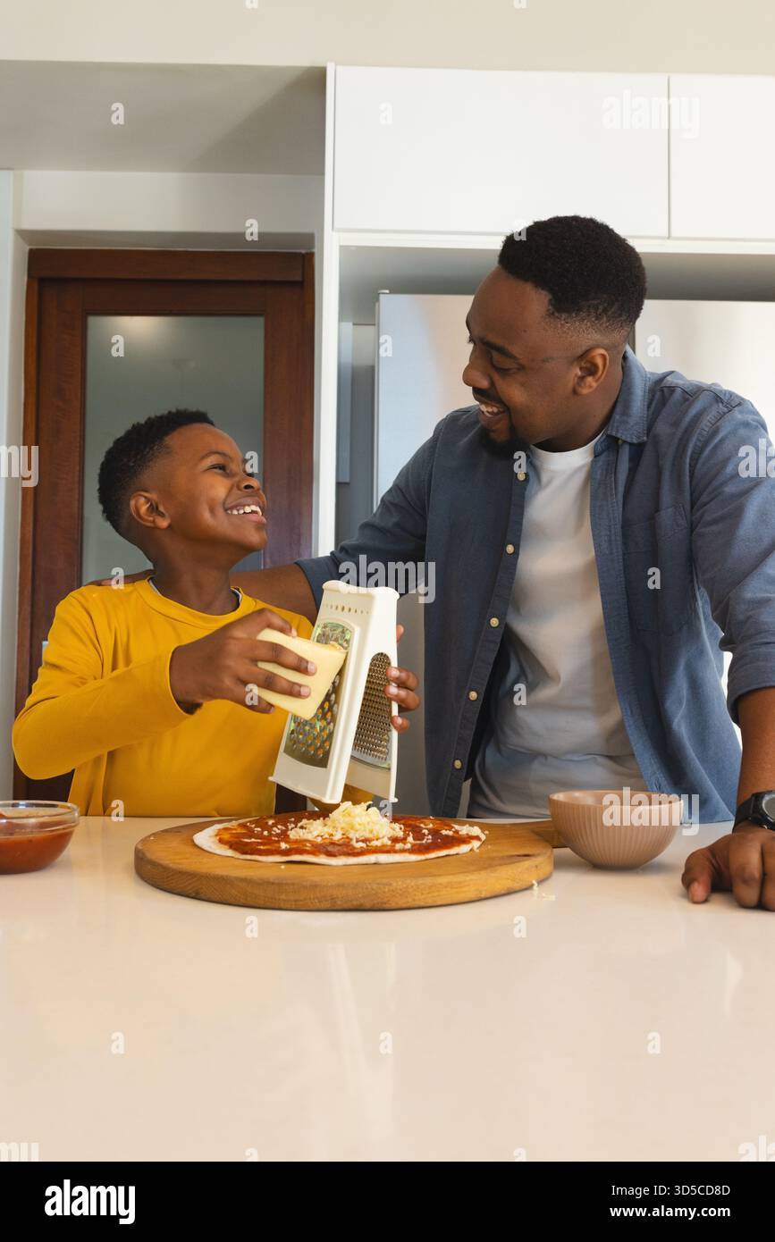 Padre e figlio fanno la pizza insieme, grattugiano il formaggio e condividono la risata Foto Stock